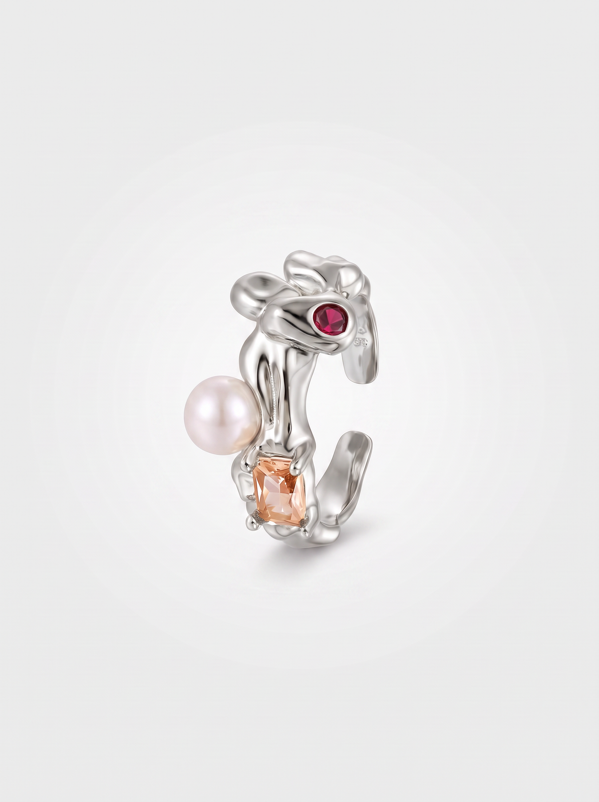 A silver-toned rabbit-shaped ring featuring a white pearl, a square peach gemstone, and a small round red gemstone, set against a light gray background.