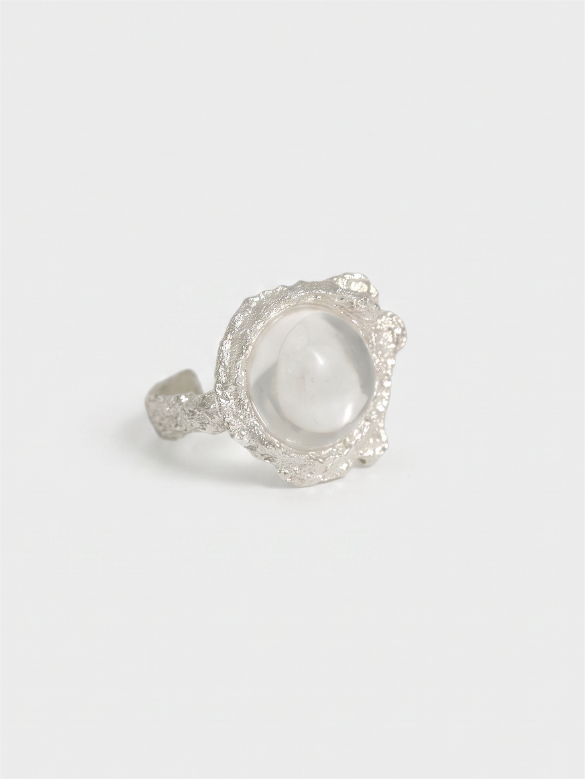 A silver ring featuring a large, smooth, oval white stone surrounded by a textured, pavé-set silver border, photographed on a clean, light gray background.