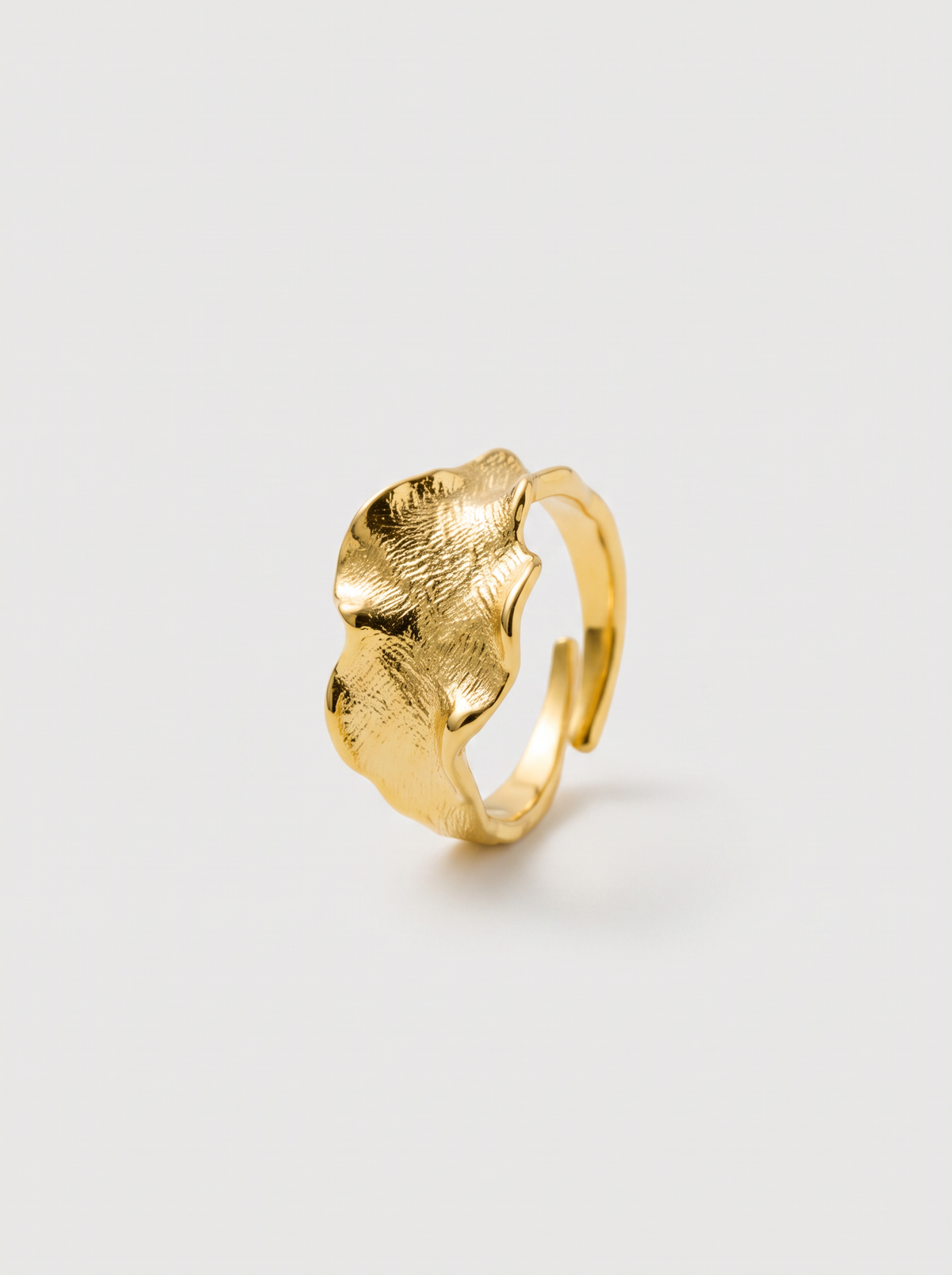 A textured gold ring with a wavy, organic leaf-like top, photographed on a clean light gray background.