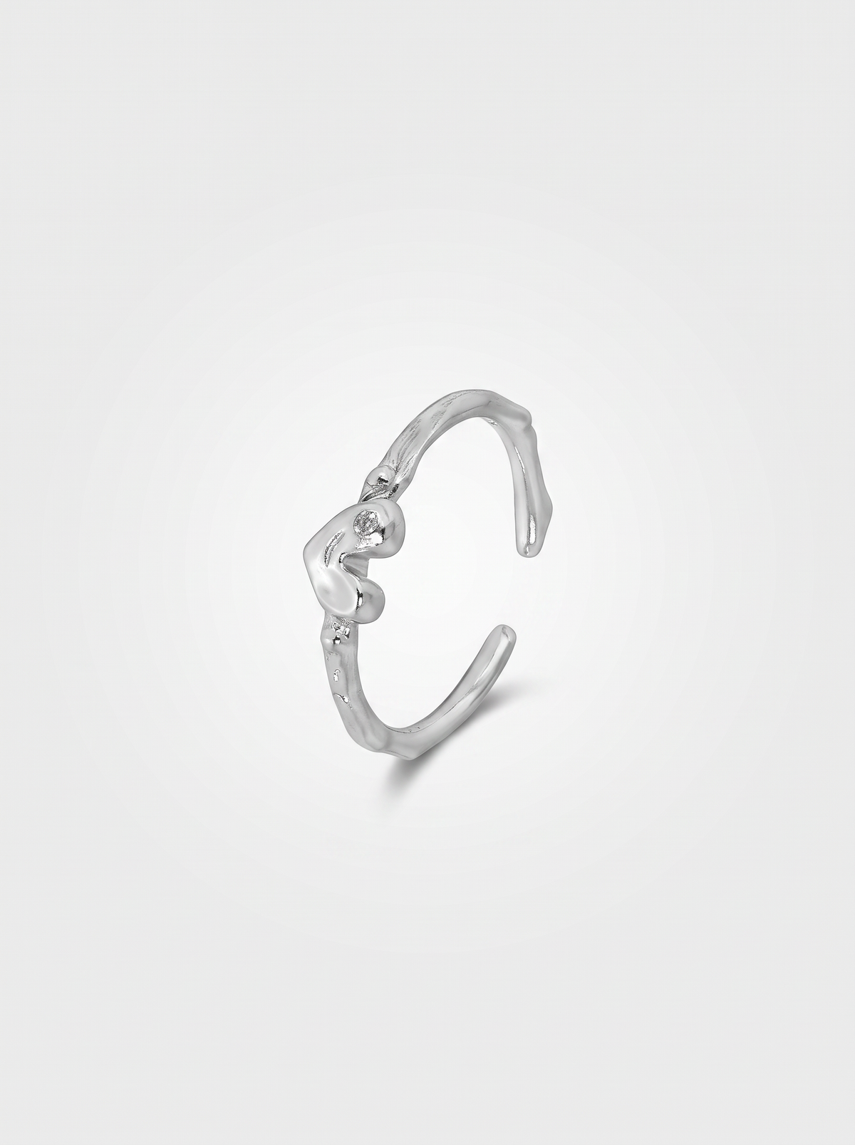 A silver-toned open cuff ring featuring a small, polished heart-shaped charm in the center, displayed on a clean, light gray background.